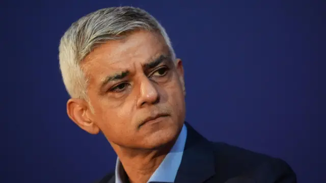 Londra Belediye Başkanı Sadiq Khan, koyu mavi bir arka plan önünde Londra'daki bir etkinlikte konuşurken görülüyor.