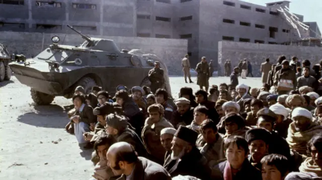 مردم در بیرون زندان پلچرخی کابل نشسته‌اند یک تانک در کنارشان 