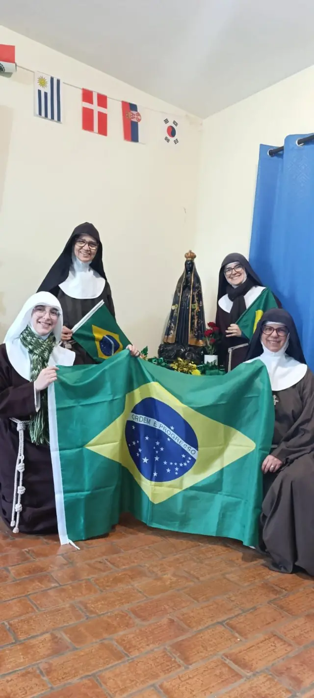 Quatro freiras seguram bandeiras do Brasil com figura de Nossa Senhora ao fundo