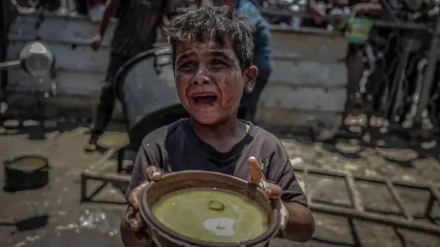Uma criança segurando um prato de comida e chorando