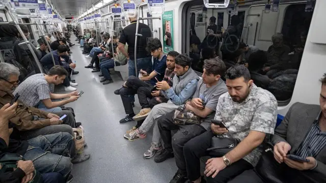 إيرانيون يمسكون هواتفهم في محطة قطار