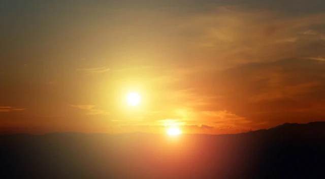 Dois sóis brilhando no céu durante o pôr do sol, com montanhas no horizonte e um céu alaranjado ao fundo.