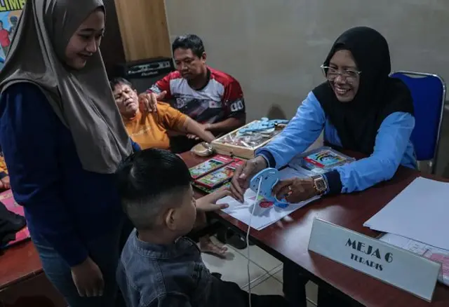 Seorang ibu (kiri) menemani anaknya selama fisioterapi oleh seorang psikiater di posyandu disabilitas di Desa Polehan, Malang, Jawa Timur, Indonesia, pada 10 Mei 2025. Semua layanan kesehatan di Posyandu (Integrated Service Post) tidak dikenakan biaya, melayani total 55 pasien dengan berbagai jenis disabilitas dan lansia