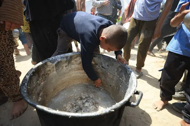 طفل فلسطيني يحاول الحصول على ما تبقى من أرز في قعر إناء فارغ