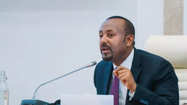 ጠቅላይ ሚኒስትር ዐቢይ አህመድ በፓርላማ ውስጥ ላይ አውራ እና አመልካች ጣቶቻቸው ገጣመው እና ቀሪዎቹ ጣቶቻቸውን አጥፈው ሲናገሩ ይታያል