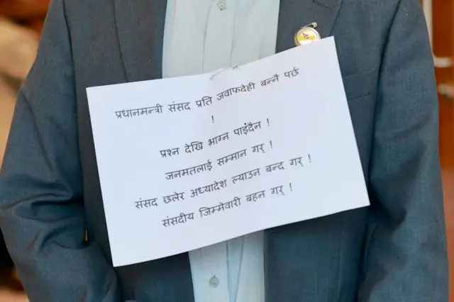 प्लाकार्ड छातीमा टाँसेका एक सांसद