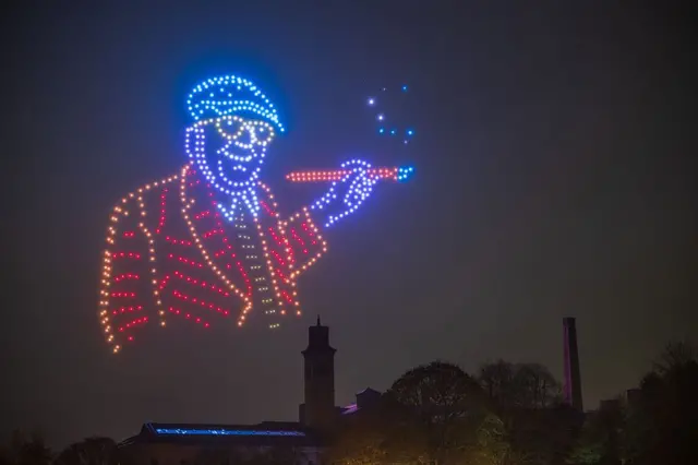 Un retrato de Hockney con sus características gafas realizado con drones en la noche.