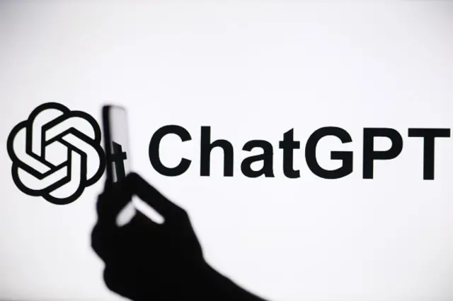 Una mano sujeta un teléfono con el logo de ChatGPT al fondo.