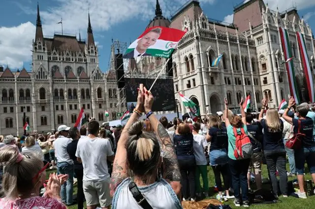 Halk parlamentonun ilk oturumunu dışarıdan izlerken, Magyar’ın portresinin bulunduğu bir bayrağı sallayan bir destekçisi, 9 Mayıs 2026. 
