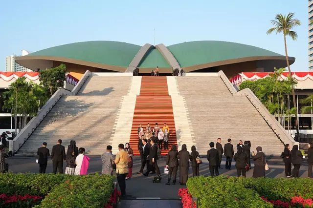 Gedung DPR di Senayan, Jakarta nampak puluhan orang berpakaian formal berada di halamannya, dan sebagian sedang mengambil foto.