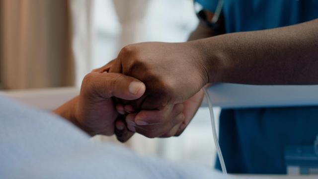 A nurse holds a paitent's hand in a hospital bed
