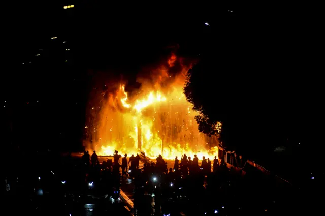 Pengunjuk rasa melihat Gerbang Tol Pejompongan yang dibakar saat aksi di Jakarta, Jumat (29/8/2025).