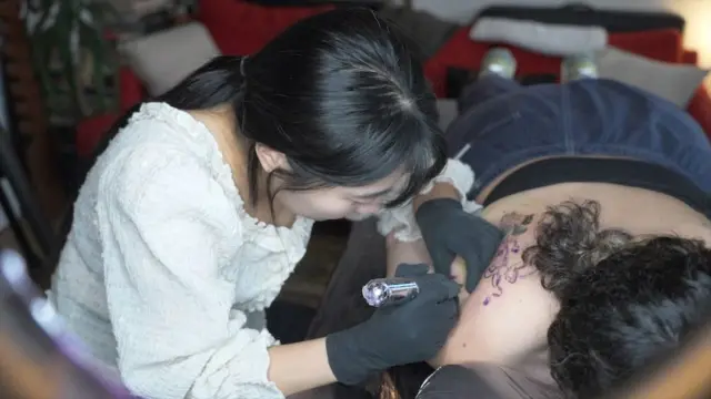 누워있는 사람의 등에 타투 시술을 하는 여성 타투이스트