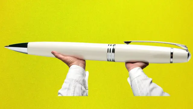 Дві руки тримають величезну кулькову ручку на жовтому тлі