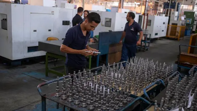 یک کارگر ایرانی در حال بررسی اجزای فلزی موتور خودرو هنگام کار در خط تولید قطعات در کارخانه خودروسازی کرمان موتور در کرمان، ایران، در تاریخ ۳ مه ۲۰۲۵.