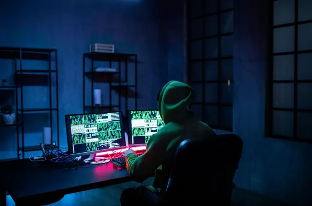 Hacker man working on computers in dark room, rear view. - stock photo