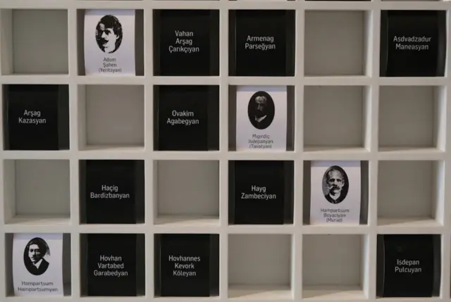24 Nisan'da tutuklanan aydınların fotoğraf ve isimlerinin yer aldığı panonun fotoğrafı. Aydınların görselleri beyaz kağıt üzerinde, sadece isimlerin yazdığı kağıtlarsa siyah renkli.