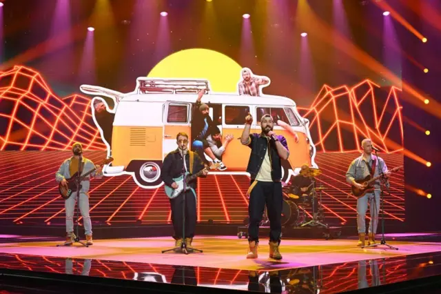 група мушкараца на сцени, тројица свирају гитаре, певач у првом плану носи качкет наопако окренут