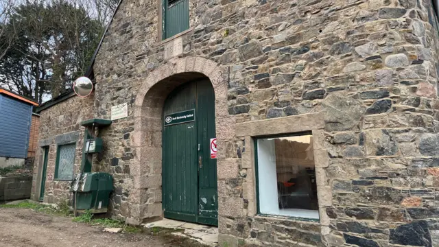 Edificio Sark Electricity: una estructura de ladrillo con una puerta verde con un cartel que dice Sark Electricity Limited.