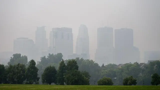 El horizonte de Minneapolis, Minnesota, está borroso por el humo, con el césped verde del parque y los árboles en primer plano.