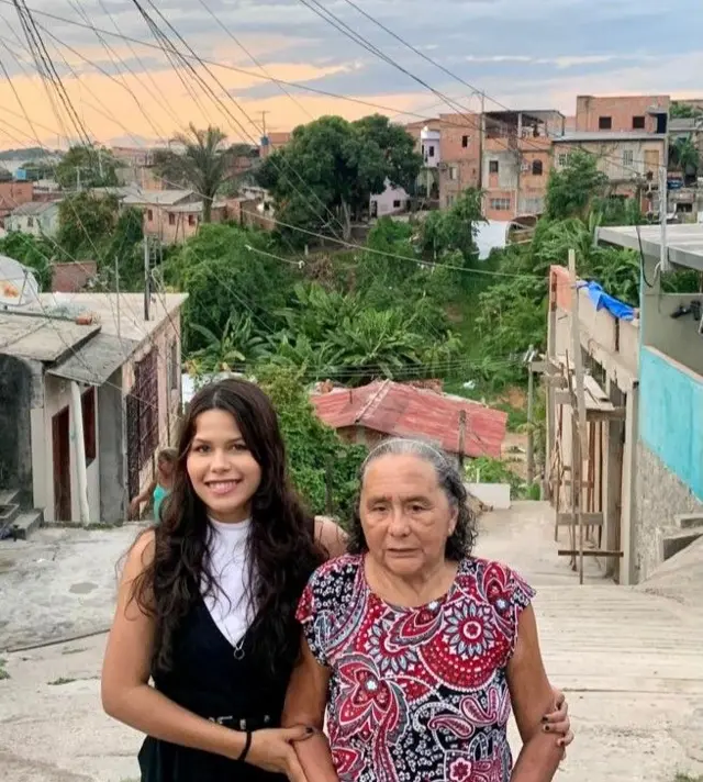 Milena Costa com a avó, dona Maria Adelaide, posam para foto na rua da casa