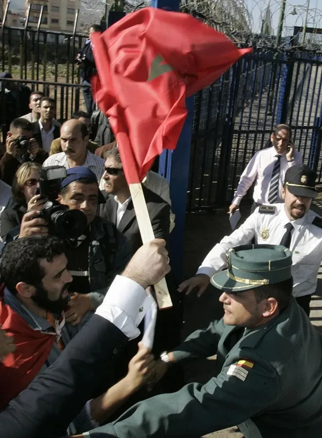 معترضان مراکشی در سمت چپ، هنگام تلاش برای ورود اجباری به خاک اسپانیا در ششم نوامبر ۲۰۰۷، با نیروهای گارد مدنی اسپانیا روبه‌رو می‌شوند. این اتفاق در شهر بنی‌انصار، در مرز منطقه اسپانیایی ملیله در شمال آفریقا، رخ داد. معترضان به سفر دوروزه خوان کارلوس و سوفیا، پادشاه و ملکه اسپانیا، به ملیله و سبته اعتراض داشتند 