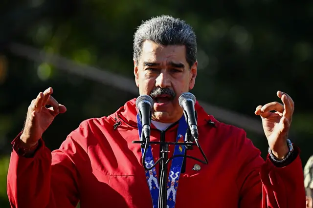 Nicolás Maduro, gesticula e discursa sob o sol, usando uma camisa vermelha, durante um comício em Caracas.