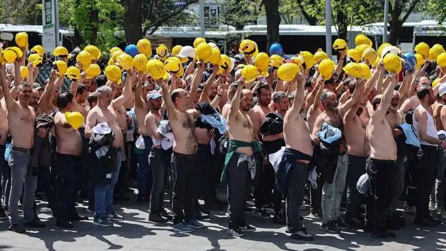 Ankara'da bir grup üstü çıplak maden işçisi sarı baretlerini havaya kaldırarak eylem yapıyor.