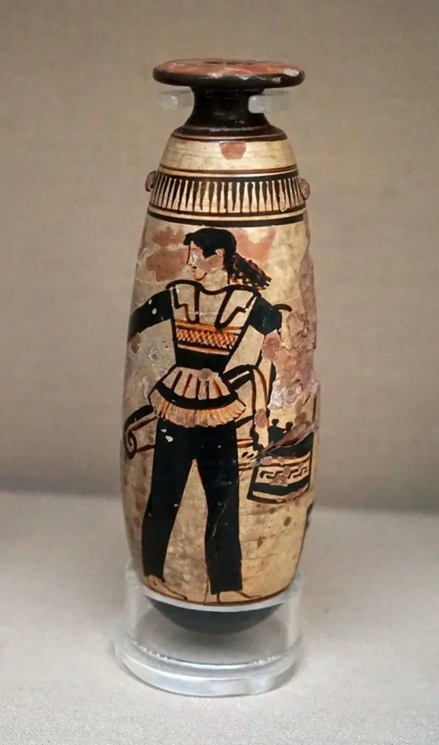 Un vaso de colores dorado y negro en el que está dibujada una mujer con unos pantalones negros