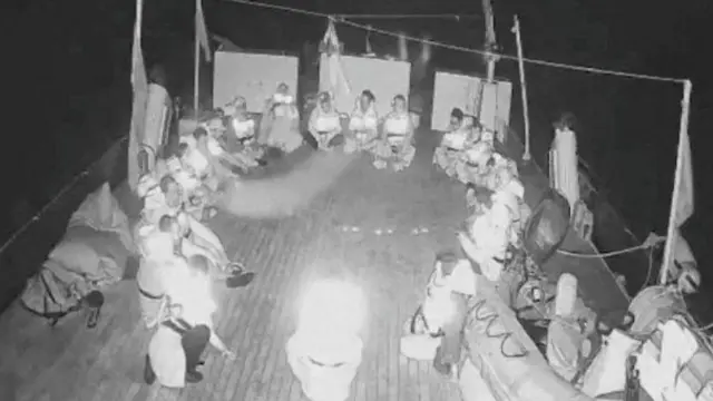 Imagem em preto e branco de baixa qualidade mostra pessoas sentadas em convés