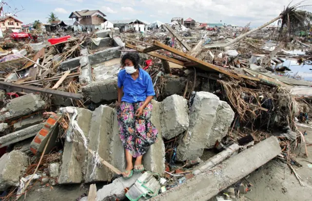 Perempuan di Aceh duduk di atas reruntuhan rumahnya yang dihancurkan tsunami 2004.
