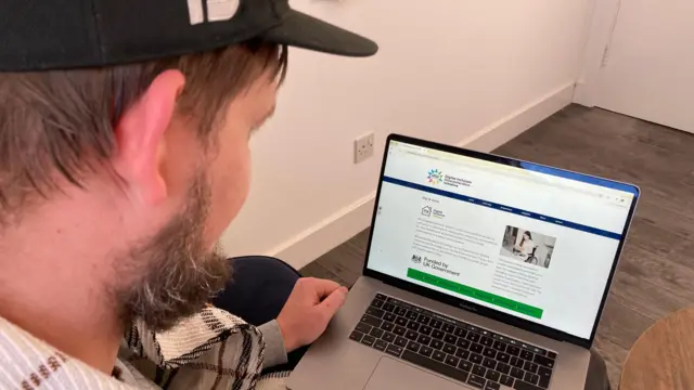 El Sr. Digby mira la pantalla de una laptop. El ángulo mira por encima del hombro hacia la pantalla, que muestra la página principal de DIGI.