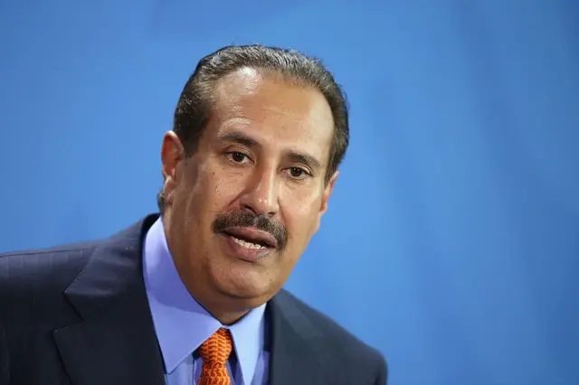 رئيس الوزراء القطري السابق، حمد بن جاسم بن جبر آل ثاني يرتدي سترة زرقاء وقميصاً أزرق يشبه لون السماء وسترة عنق برتقالية اللون.