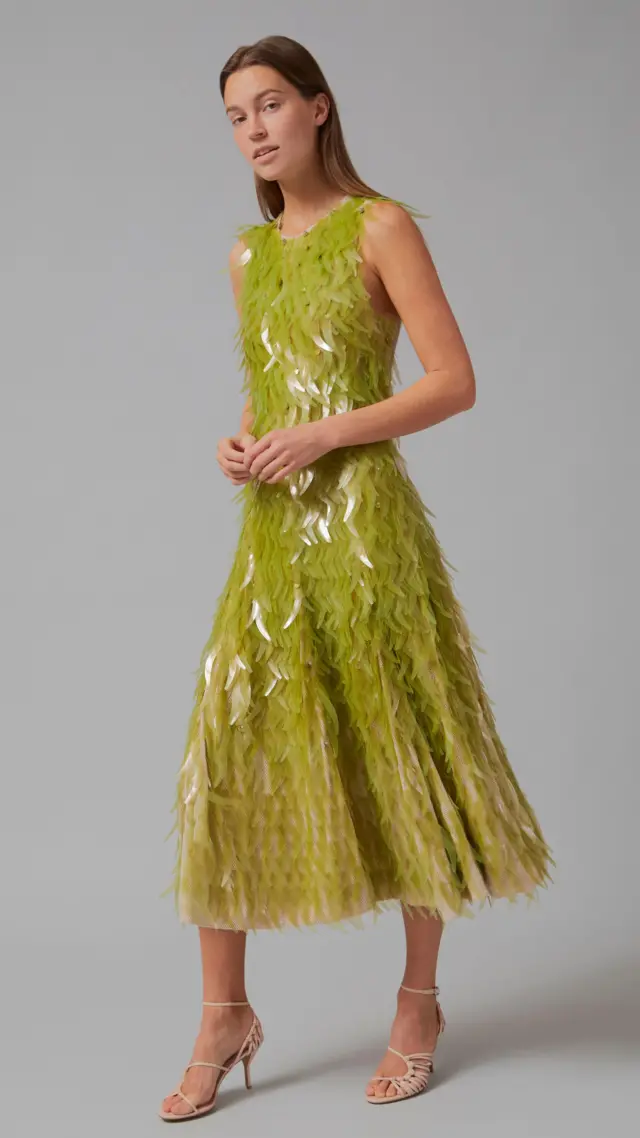 Kadın manken, pullarla süslenmiş, parıldayan orta boy yeşil bir elbiseyle poz veriyor.