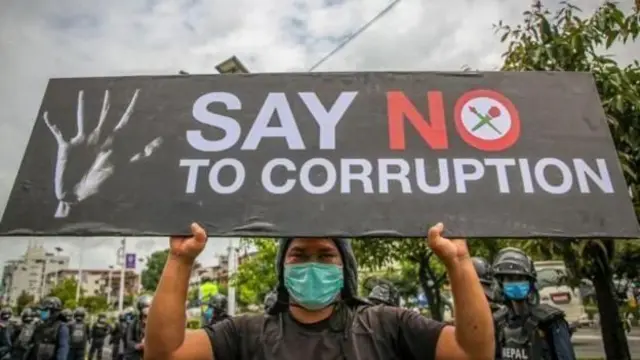 भ्रष्टाचारविरोधी प्लेकार्ड बोकेर उभिएका एक प्रदर्शनकारी र पृष्ठभूमिमा प्रहरी