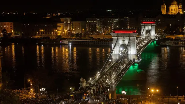 Multitudes cruzan el Puente de las Cadenas iluminado con luces verdes, rojas y blancas durante la noche de las elecciones generales en Budapest.