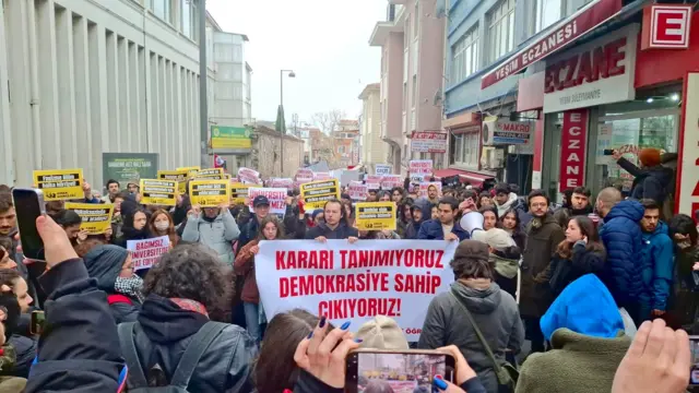 Öğrenciler ellerinde pankart ve dövizlerle poz veriyor.

Ortadaki pankartta 