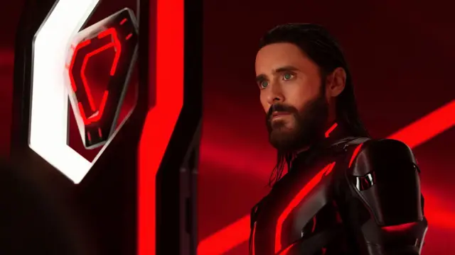 Кадр із фільму "Трон: Арес" - чоловік в чорних обладунках на червоному тлі, поряд футуристична конструкція