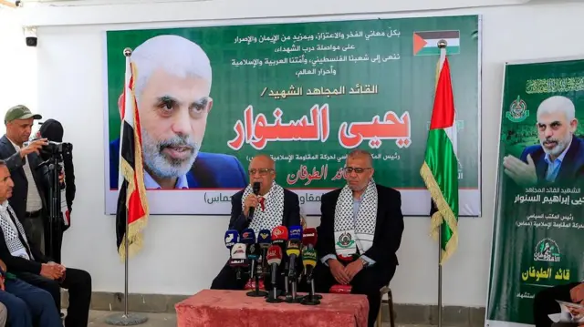 نخست وزیر حوثی های یمن و چندین نفر دیگر نشسته در مقابل تصویری از یحیی سنوار