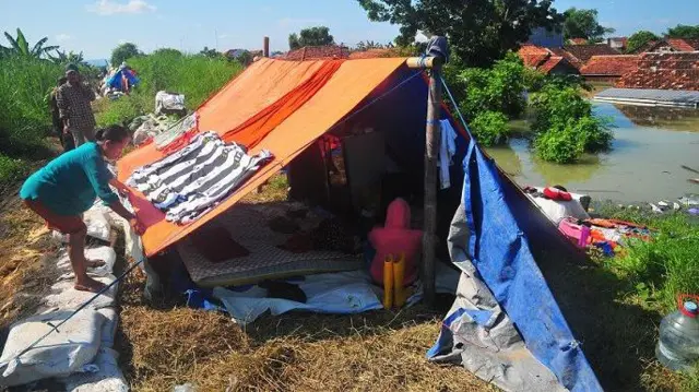 Warga menjemur pakaian di tenda darurat di tanggul sungai saat mengungsi dari banjir di Karanganyar, Demak, Jawa Tengah, Jumat (9/2/2024).