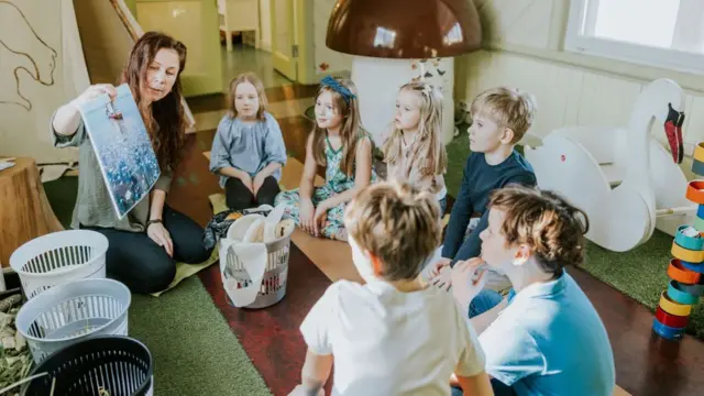 Professora sentada no chão com gruposinais aviator betnacionalcrianças mostrando como reciclar o lixo na Estônia