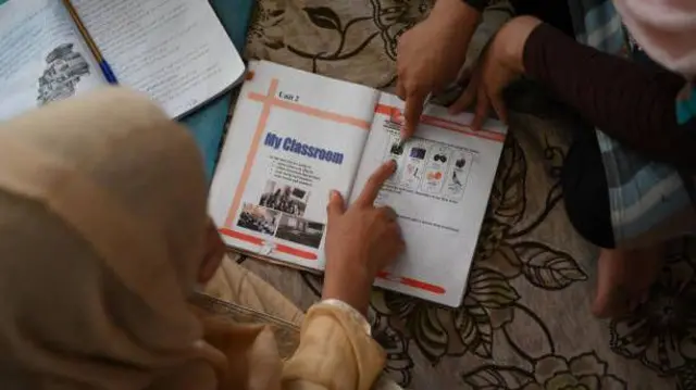 نمای دو دختر که در حال خواندن از روی یک کتاب درسی انگلیسی هستند. این تصویر از بالای سر این دختران گرفته شده و چهره شان در تصویر هویدا نیست.