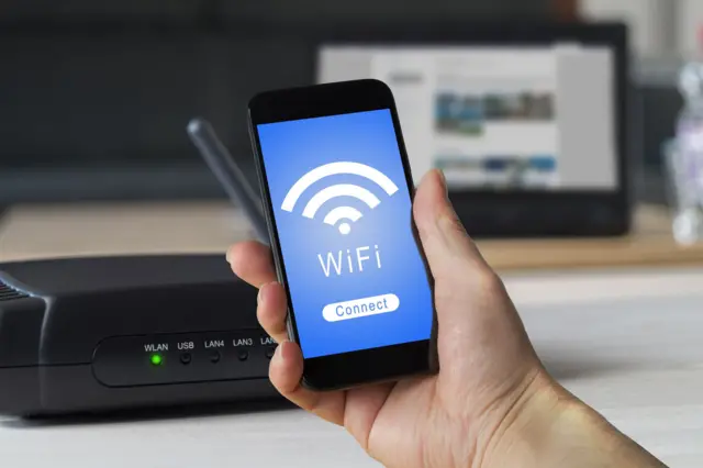 Wi-Fi රවුටර් එකක් සහ ජංගම දුරකථනයක් අතින් අල්ලාගෙන සිටින අයෙක්