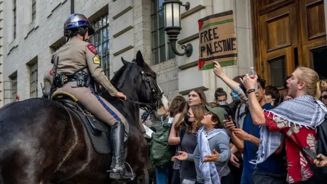 Um policial a cavalo na frentedubai bet365manifestantes, um deles segura uma faixa "Palestina Livre"