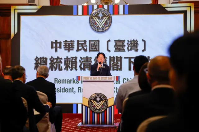 台湾总统赖清德在台上演说，一些宾客背对镜头坐下聆听赖清德发言。