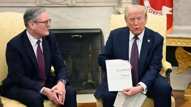 O presidente dos EUA, Donald Trump, segura uma carta do rei Charles 3º durante reunião bilateral com o primeiro-ministro britânico, Keir Starmer, no Salão Oval. Ambos vestem trajes azul-escuros e estão sentados em poltronas com estofamento creme