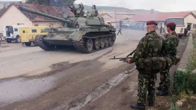 A Serbian tank and its crew drive past standing British soldiers in Kosovo