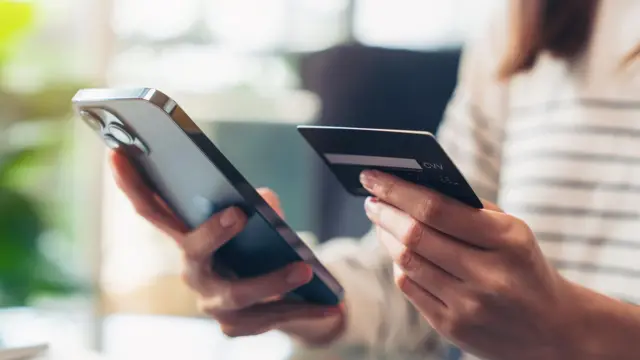 左手にクレジットカードを、右手にスマートフォンを持つ女性