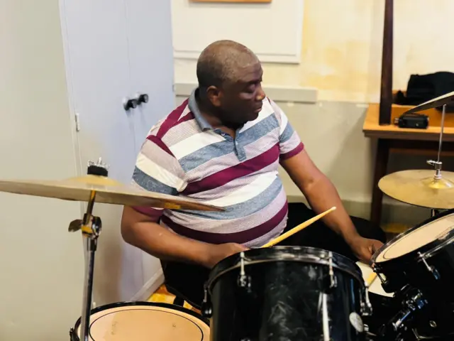 Emmanuel Sadiki batazira Kirokiro yicaye arimo kuvuza ingoma za kizungu. 