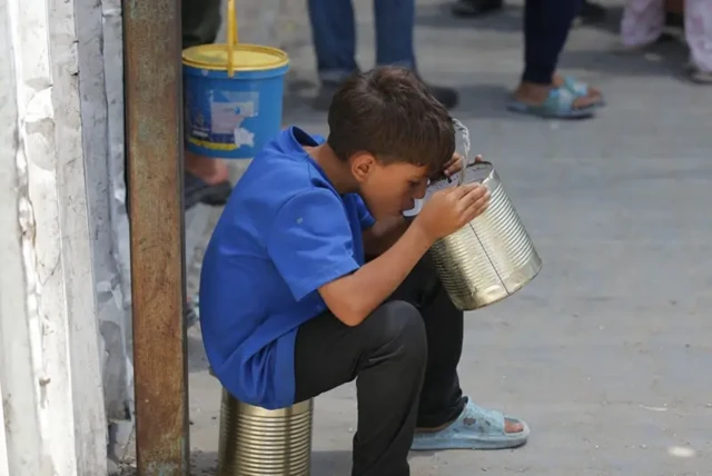 یک کودک در کوچه نشسته و از سطل غذا میخورد